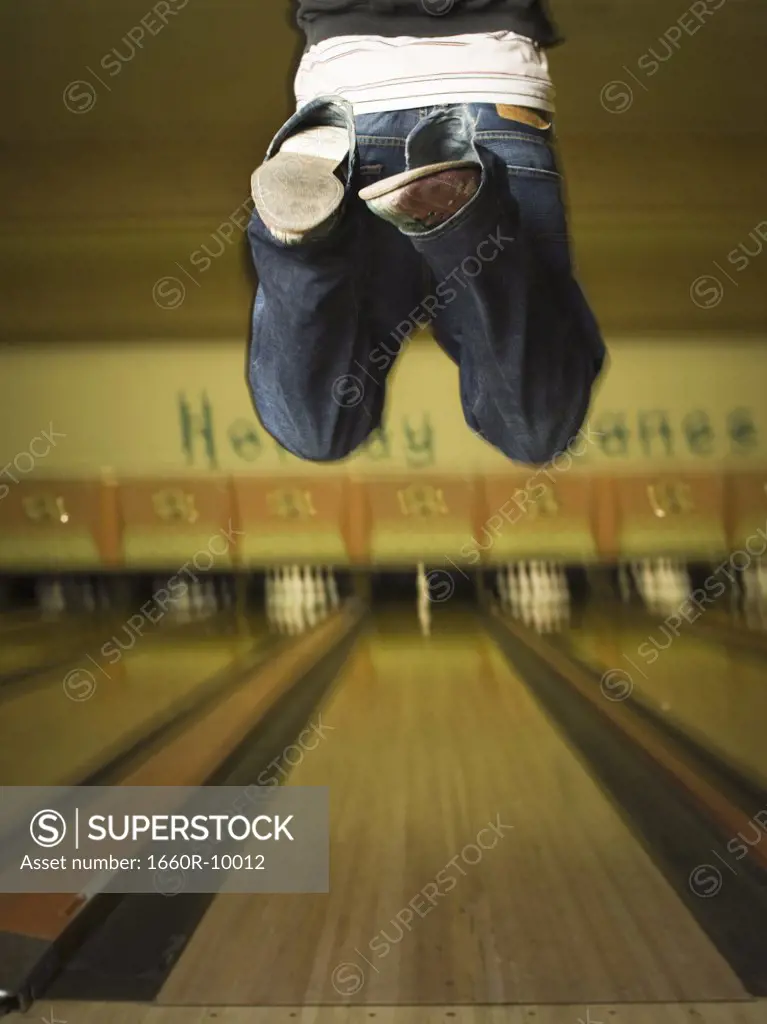 Low section view of a young man jumping at a bowling alley