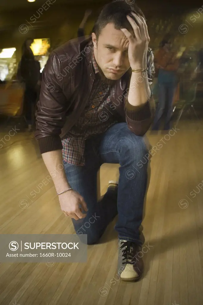 Young man kneeling with his hand on his forehead at a bowling alley