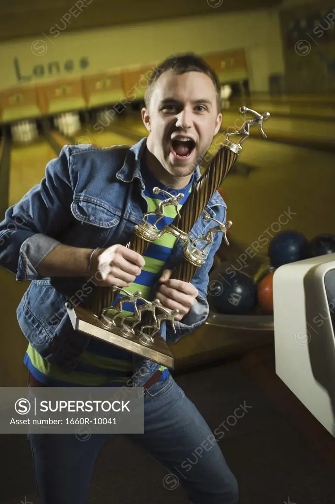 Portrait of a young man holding a bowling trophy and dancing