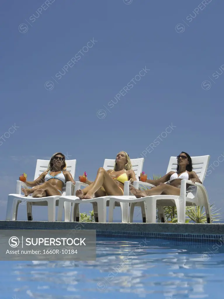 Three young women sunbathing by the pool