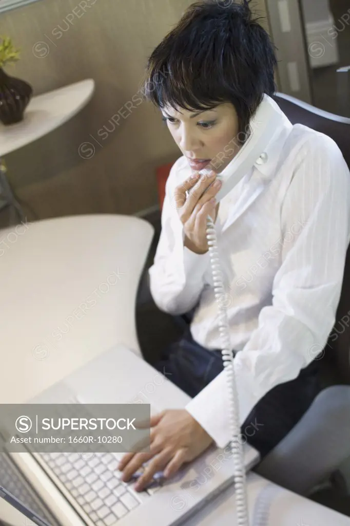 High angle view of a businesswoman using a laptop and talking on the telephone