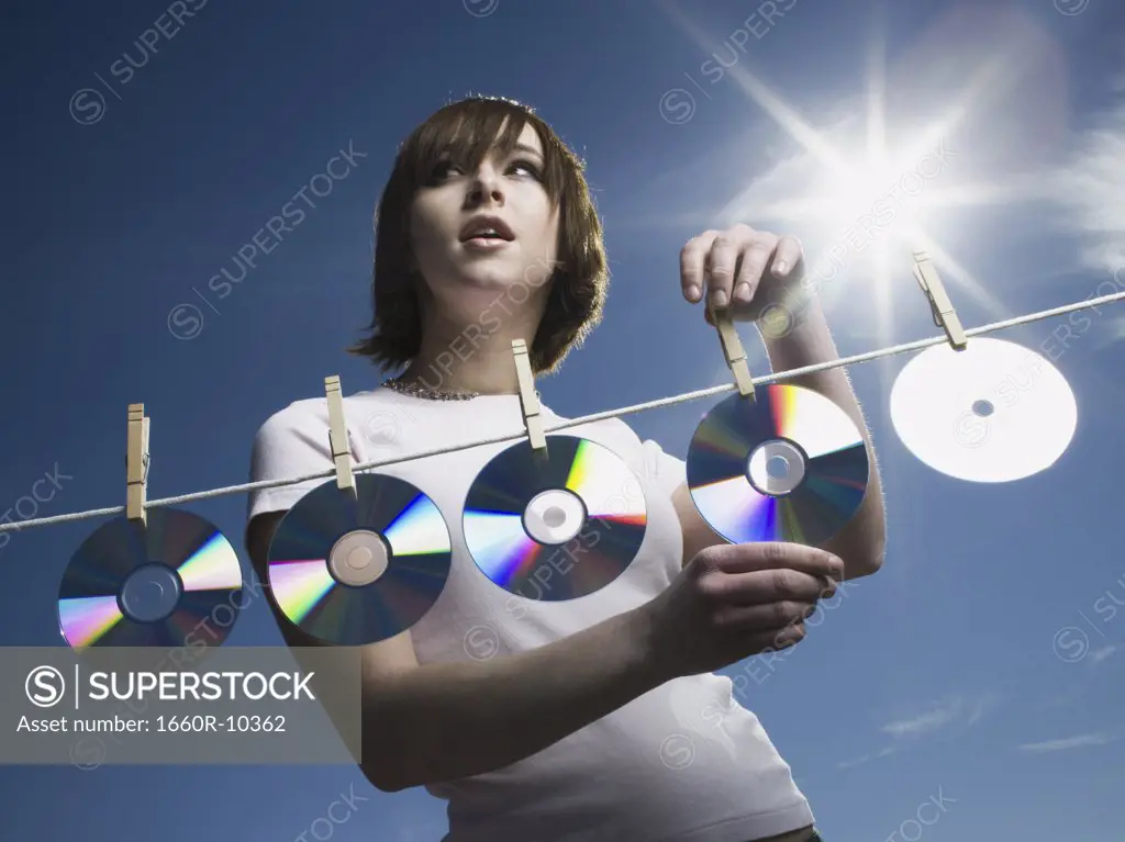 Low angle view of a teenage girl drying CDs on a clothesline