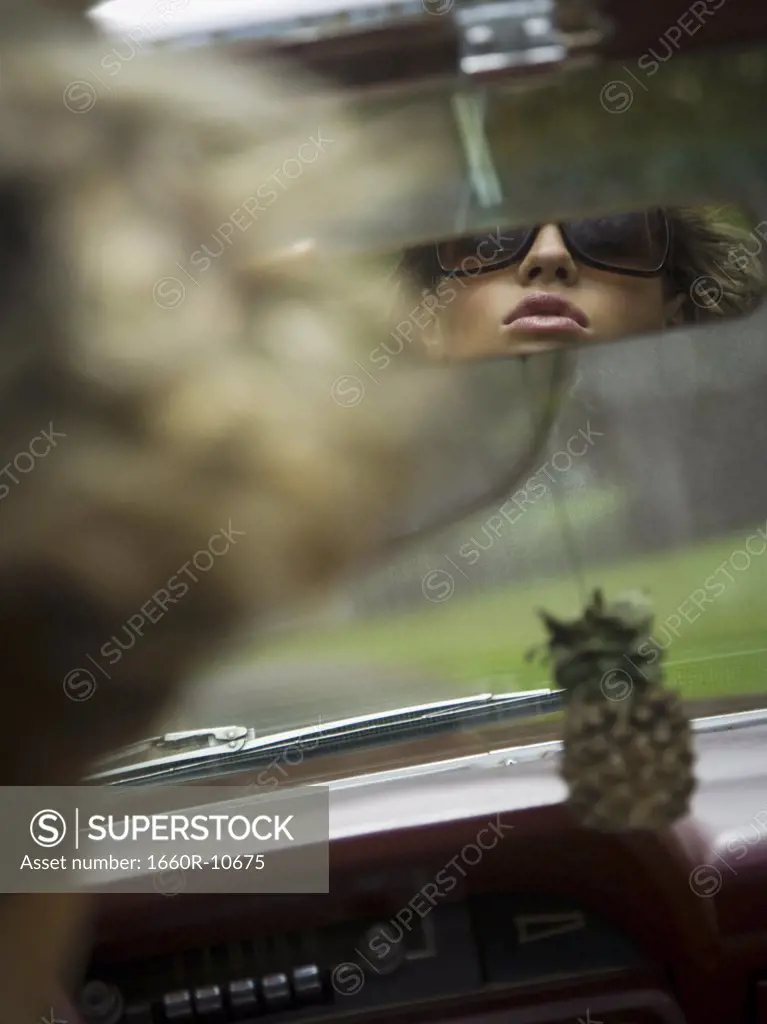 Reflection of a young woman in the rear view mirror of a car