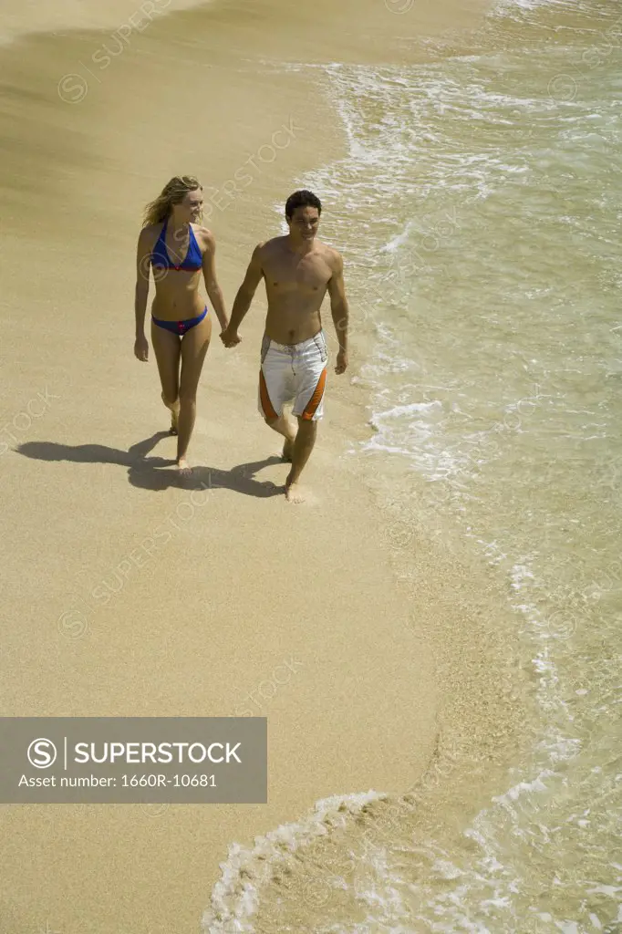 High angle view of a young couple holding hands and walking on the beach