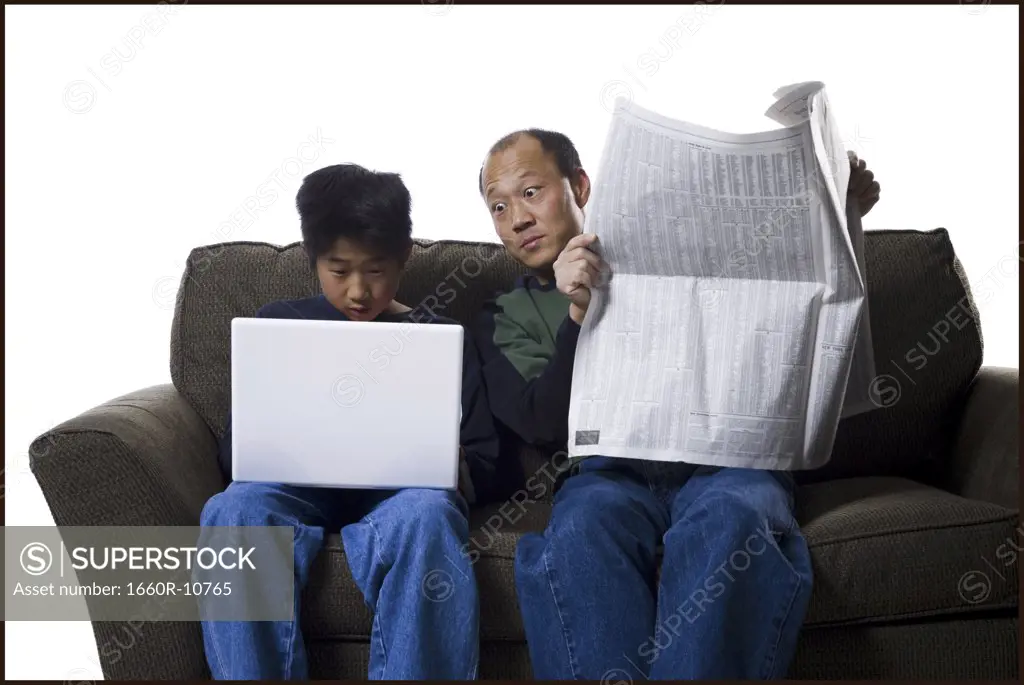 Close-up of a father holding a newspaper and his son using a laptop