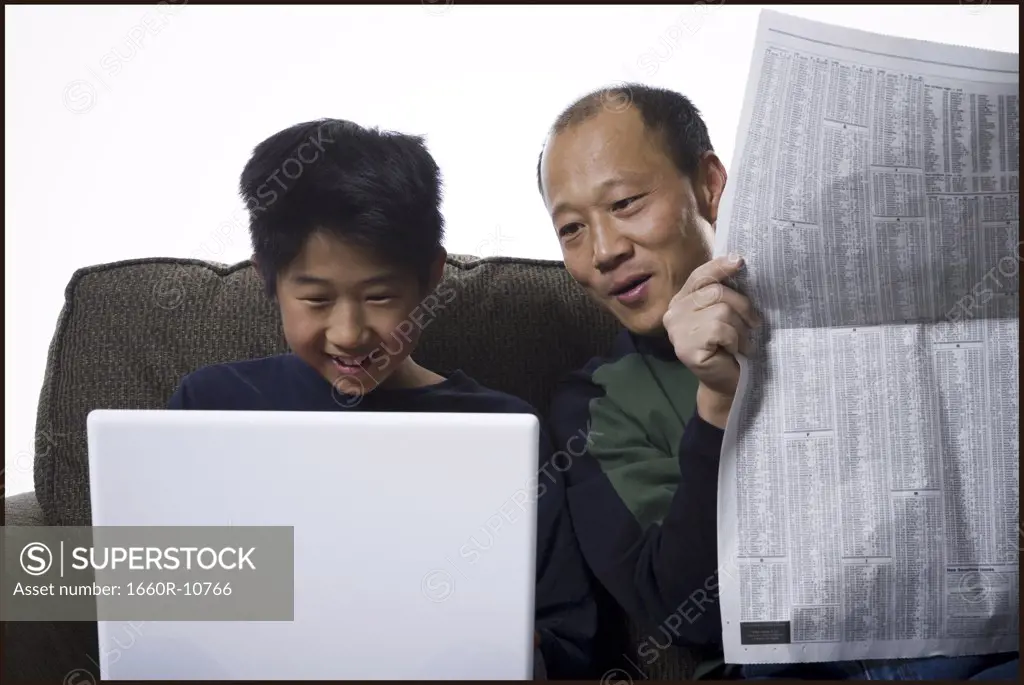 Close-up of a father holding a newspaper and his son using a laptop