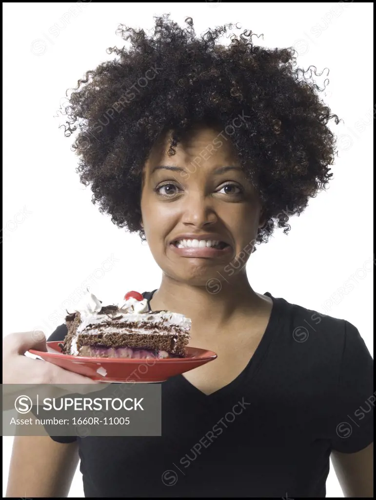 Portrait of a young woman making a face with a person holding a cake in front of her