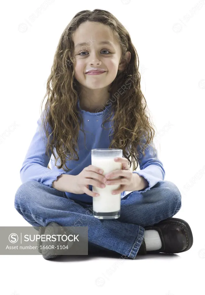 Portrait of a girl sitting on the floor and holding a glass of milk