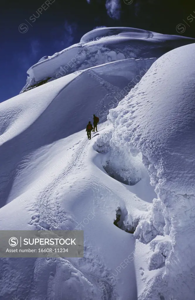 High angle view of two hikers climbing on snowy mountain peak