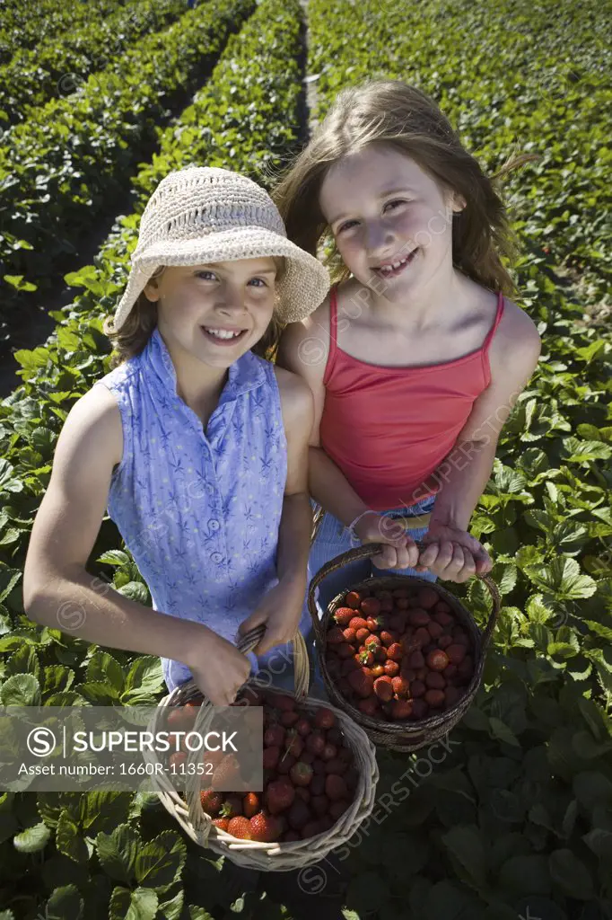 Portrait of two girls with baskets of strawberries on a field