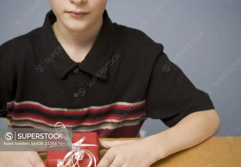 Mid section view of a boy sitting at the table holding a gift