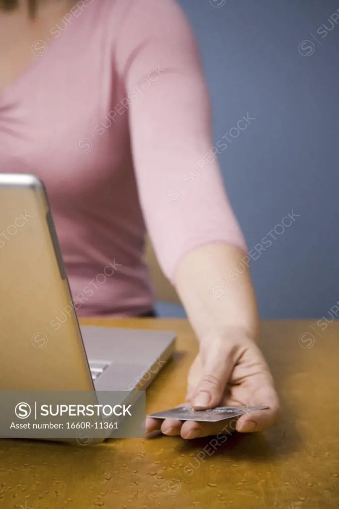 Mid section view of a woman using a laptop and holding a credit card