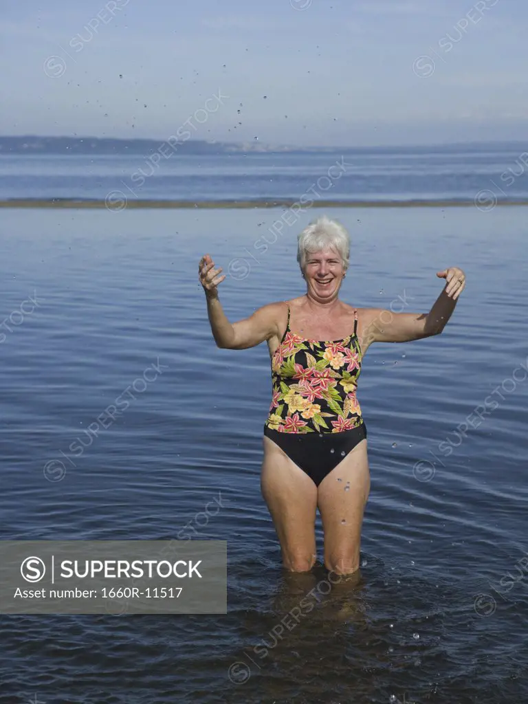 Portrait of a mature woman standing in water with her arms raised