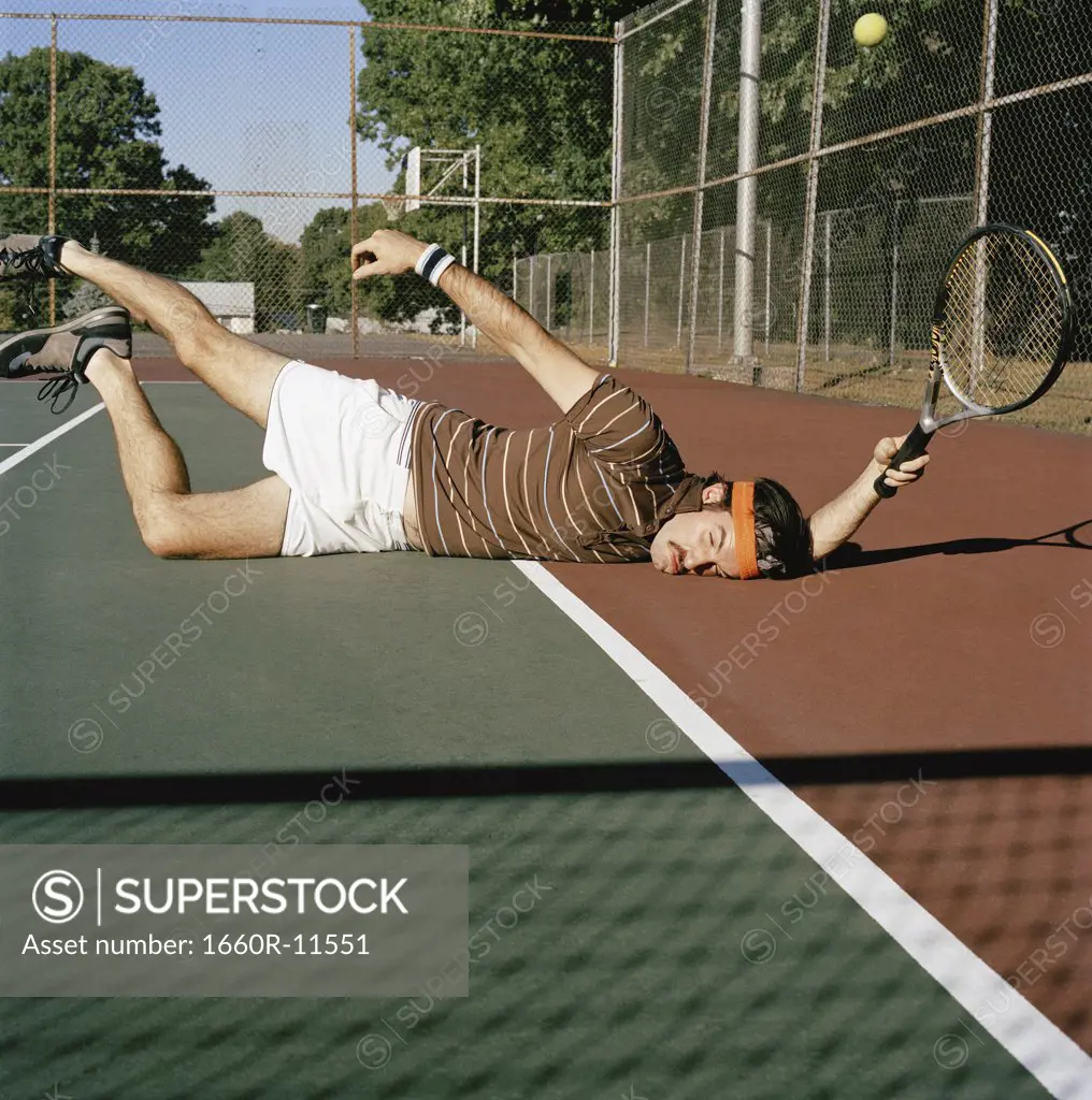 Young man falling down on a tennis court