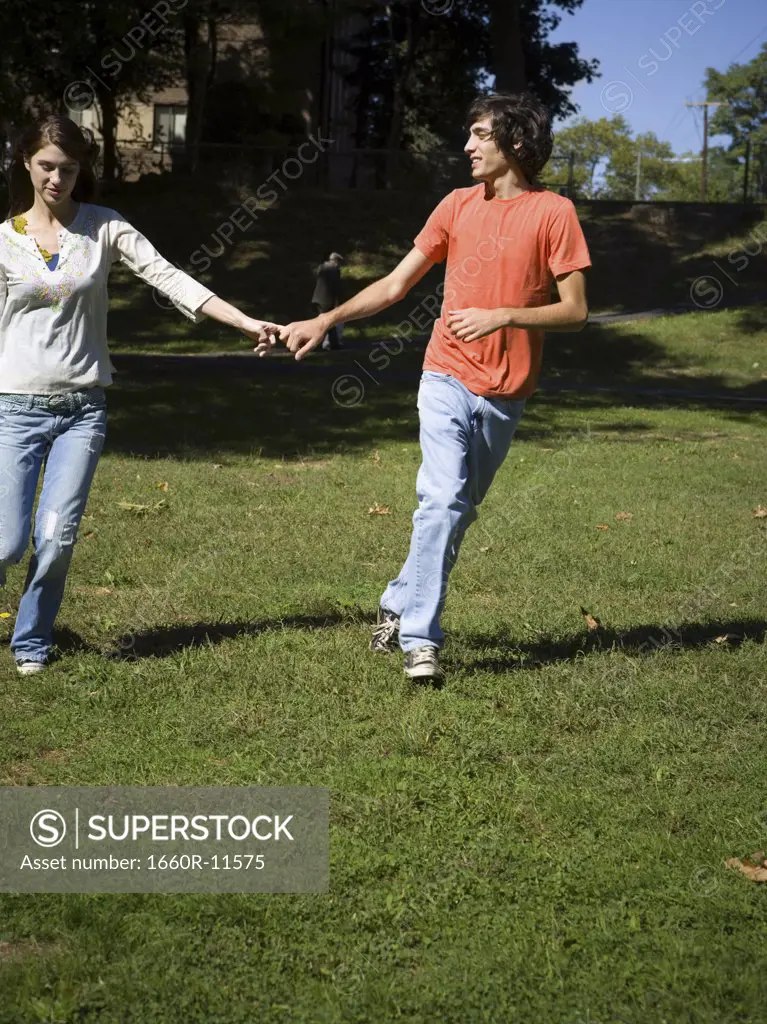 Teenage couple holding hands running in the park