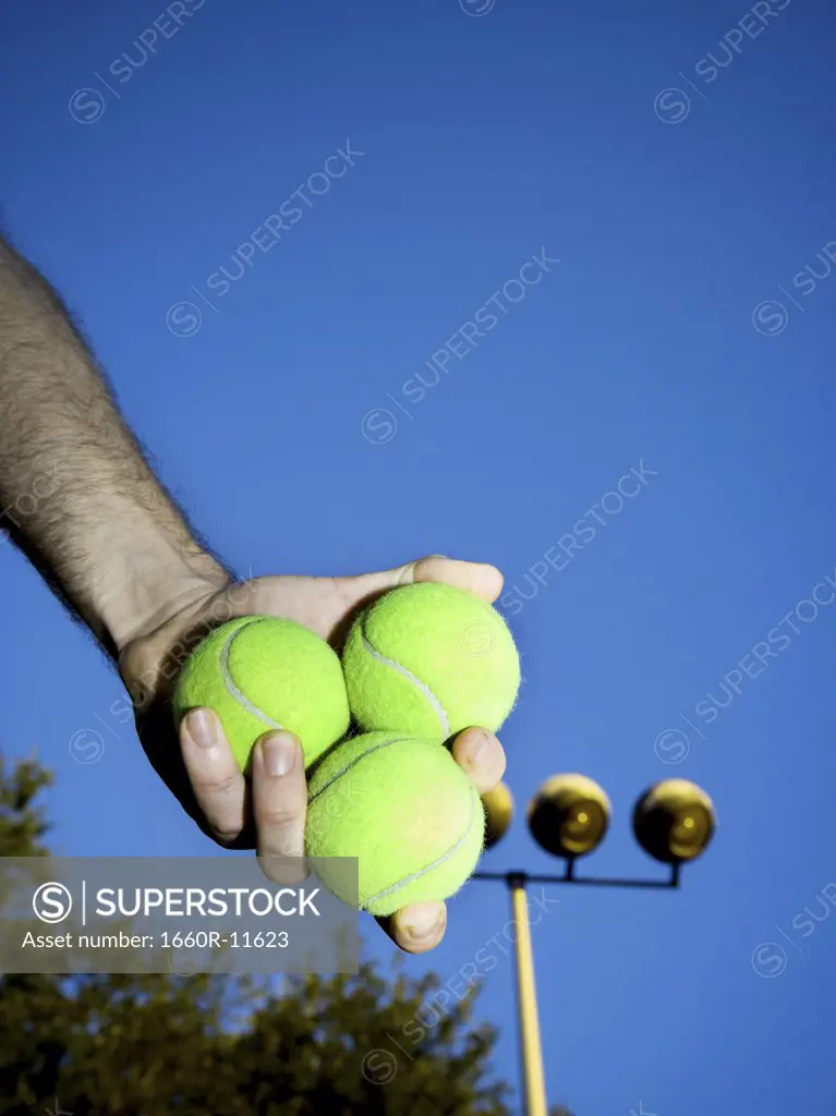 Low angle view of a person holding three tennis balls