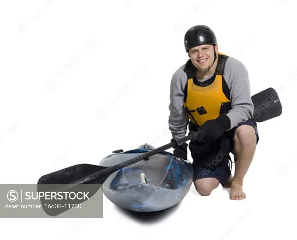 Portrait of a young man kneeling beside a kayak