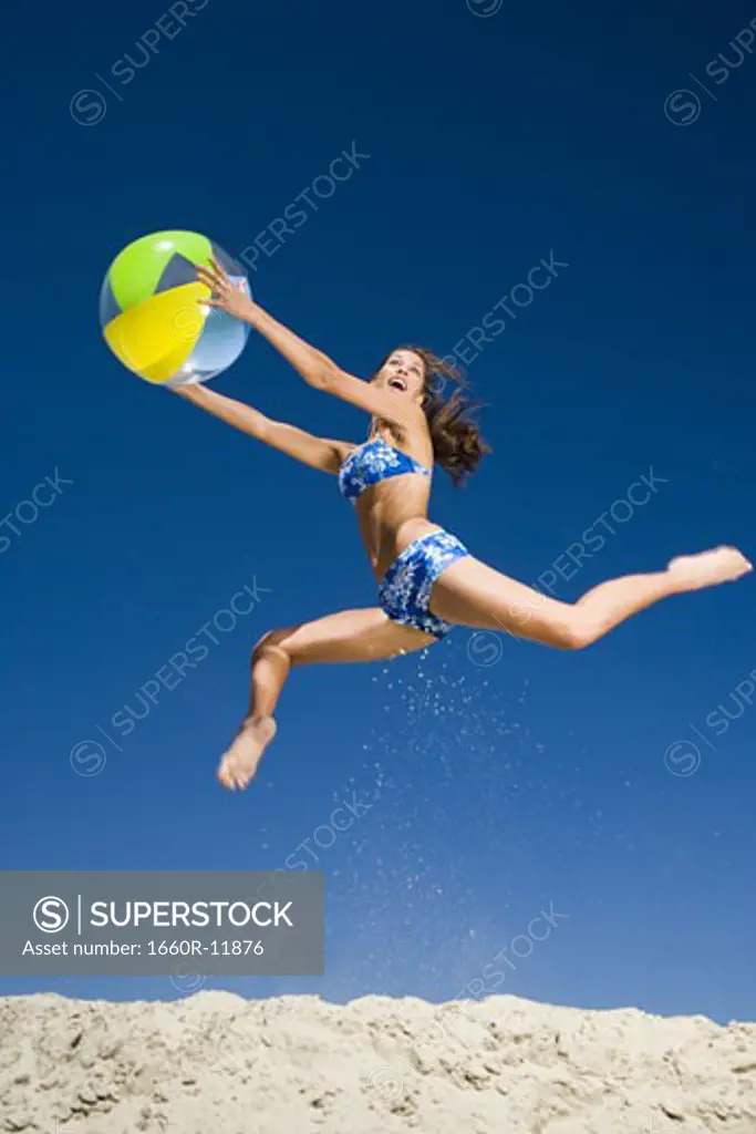 Young woman holding a beach ball and jumping