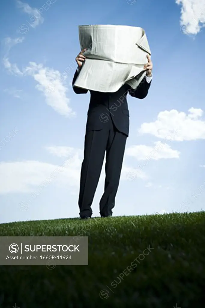 Businessman standing on the grass and reading a newspaper