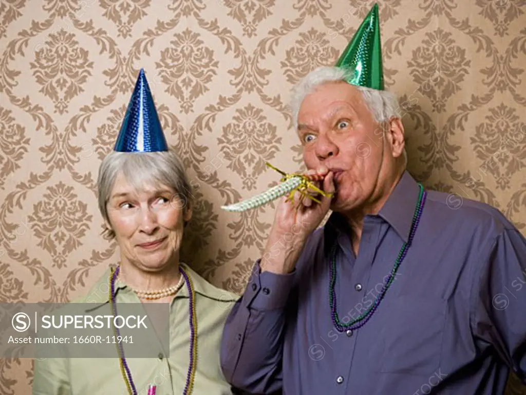 A senior man standing with a senior woman and blowing a party favor