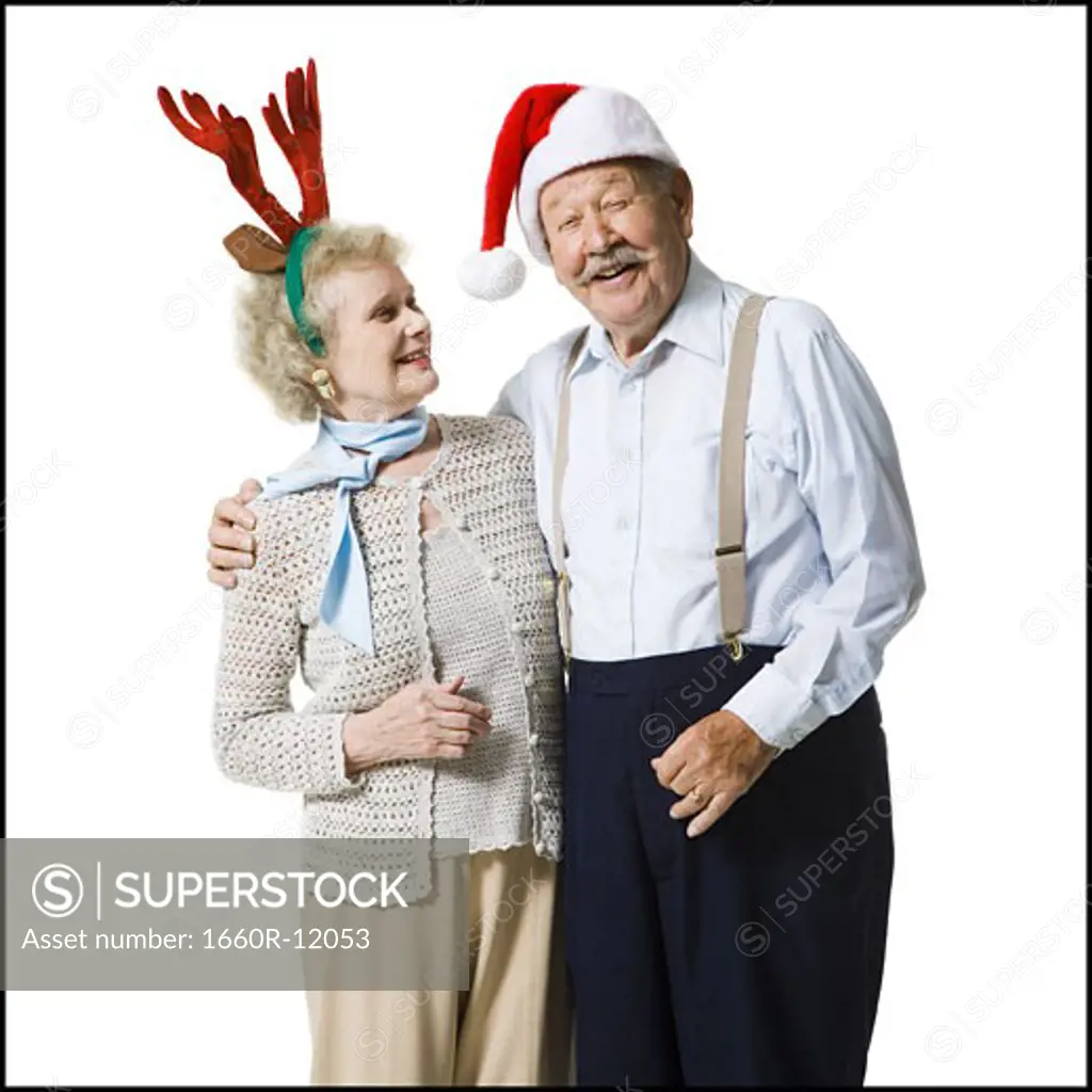 An elderly couple wearing Christmas hats laugh together