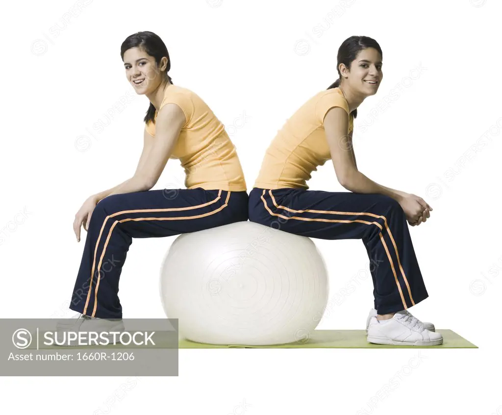 Profile of two twin teenage girls sitting on a fitness ball