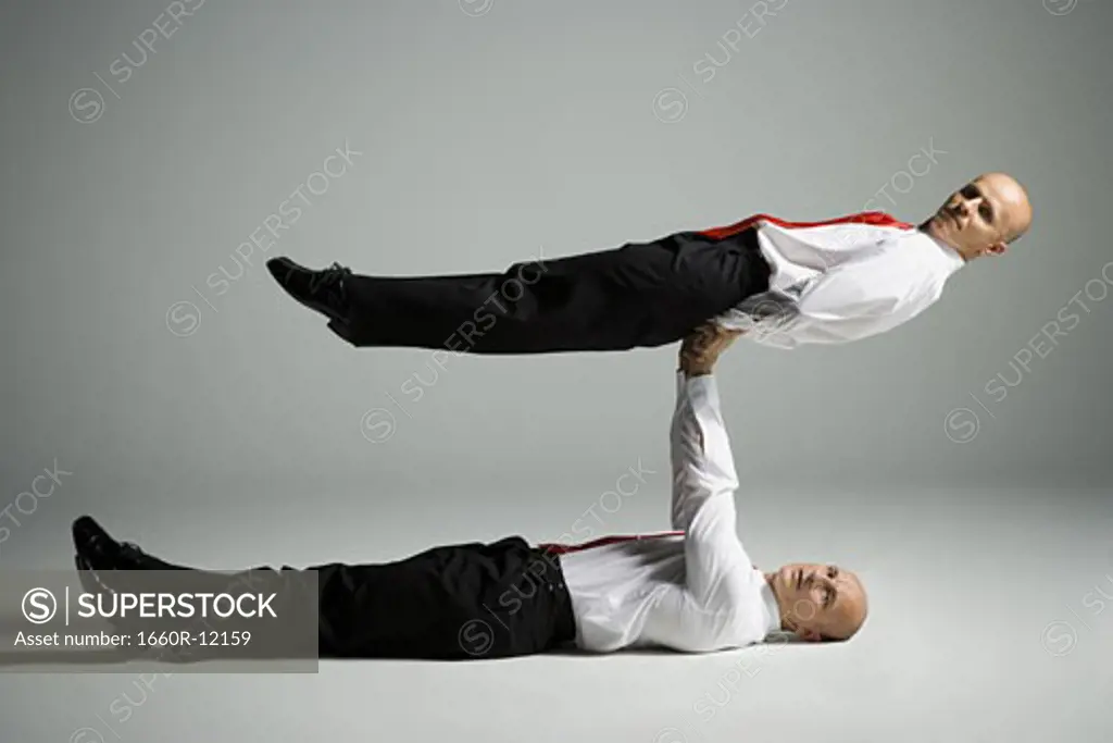Profile of two male acrobats in business suits performing