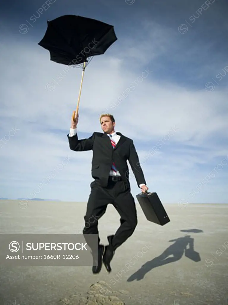 Businessman jumping while holding an umbrella and a briefcase