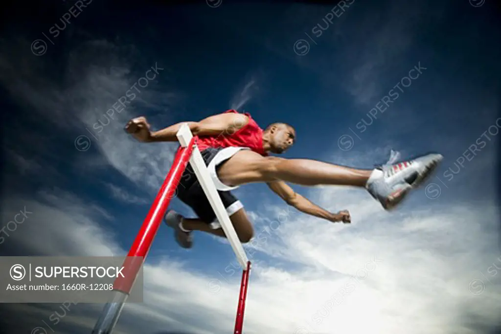 Low angle view of a young man jumping over a hurdle in a race