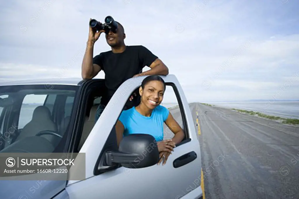 Young woman smiling with a young man looking through a pair of binoculars