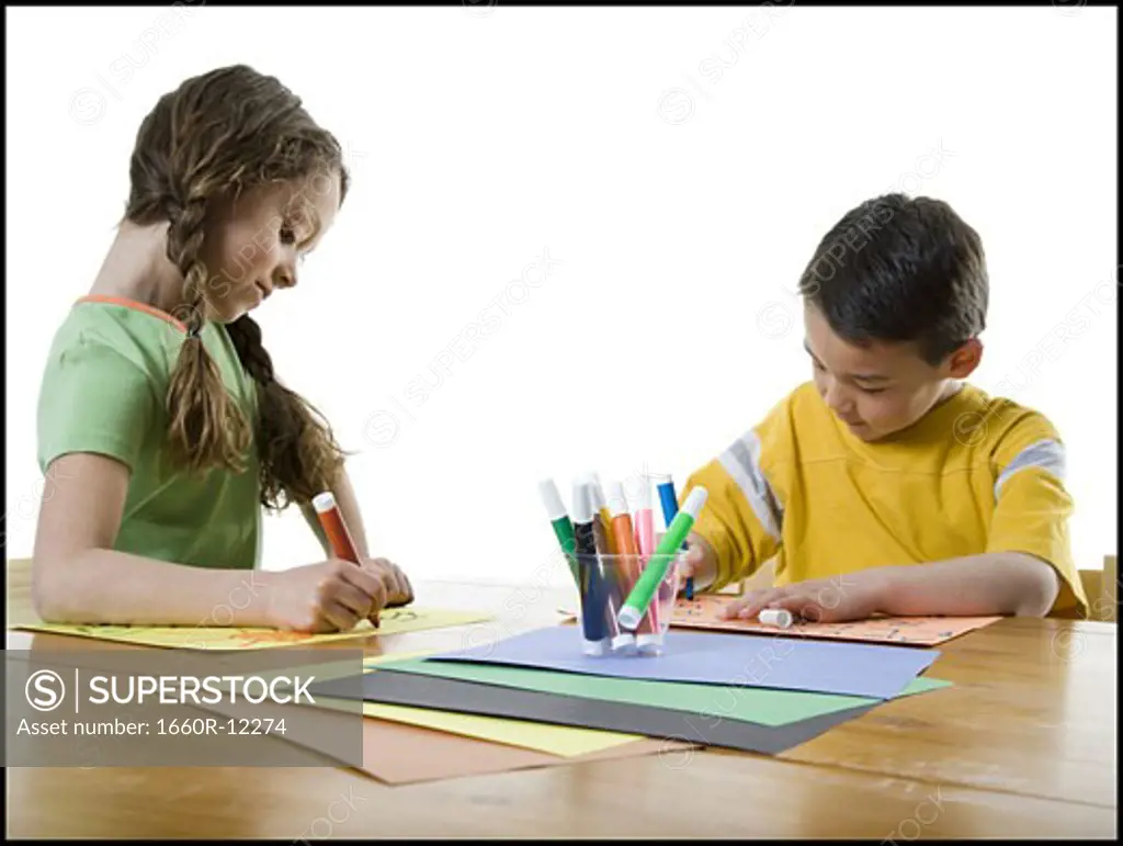 Close-up of a girl and her brother drawing on papers with felt tip pens