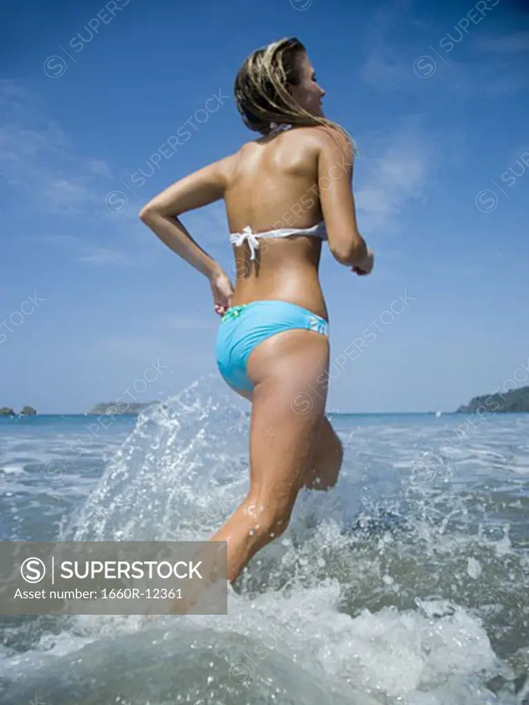Rear view of a young woman running in water on the beach