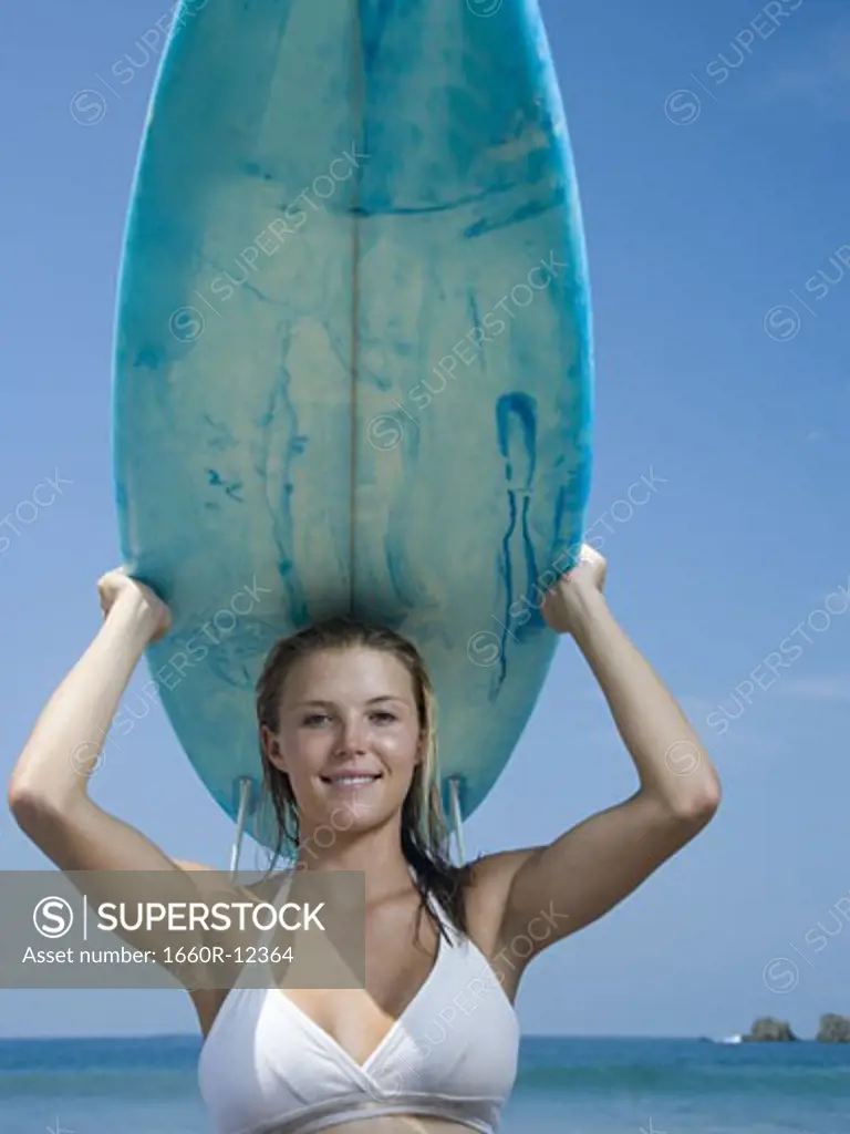 Portrait of a young woman holding a surfboard over her head