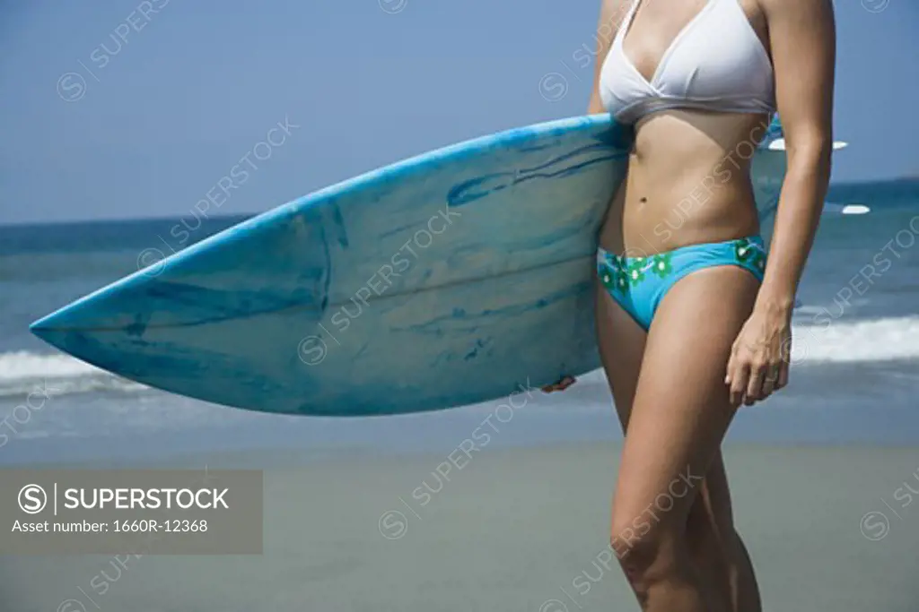 Mid section view of a young woman holding a surfboard