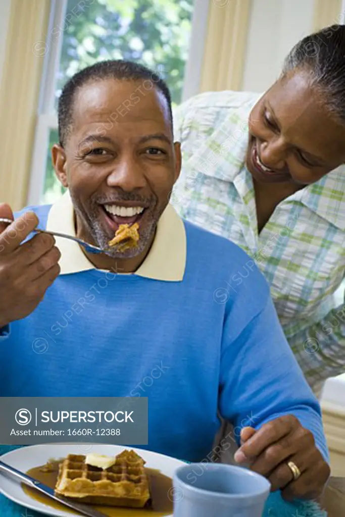 Close-up of a senior man having breakfast with a senior woman behind him