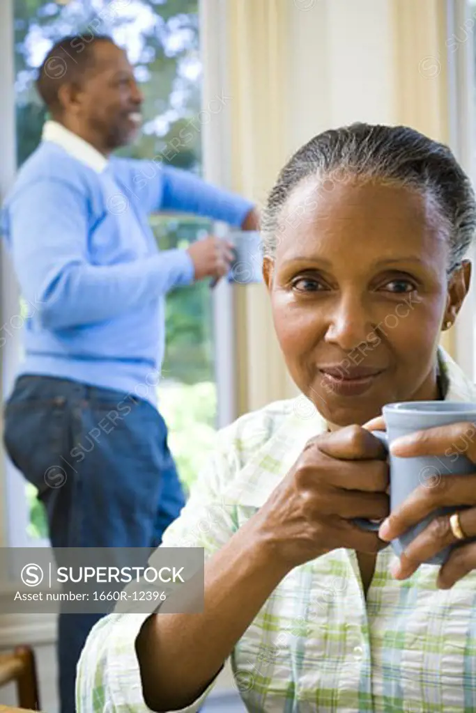Close-up of a senior woman holding a cup of coffee with a senior man standing behind her