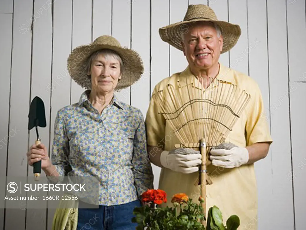 Portrait of an elderly couple standing with gardening tools
