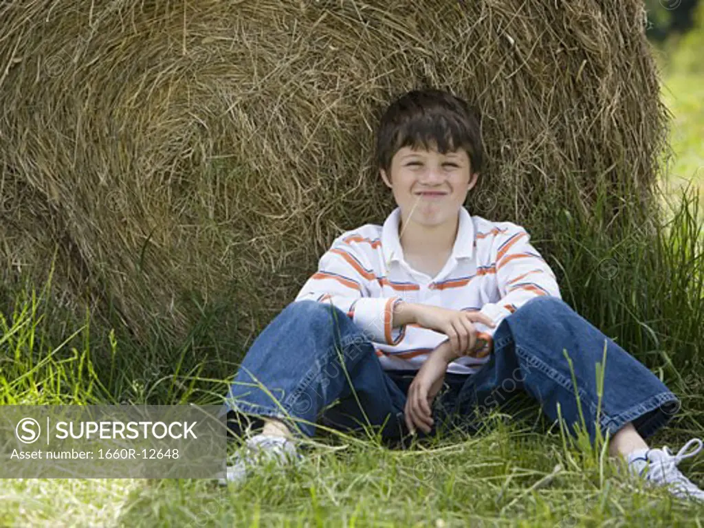 Portrait of a boy sitting against a hay bale