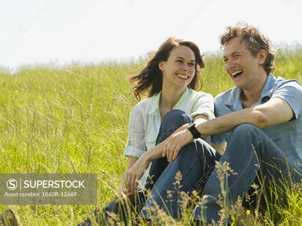 Close-up of a woman and a man sitting together and laughing in a field
