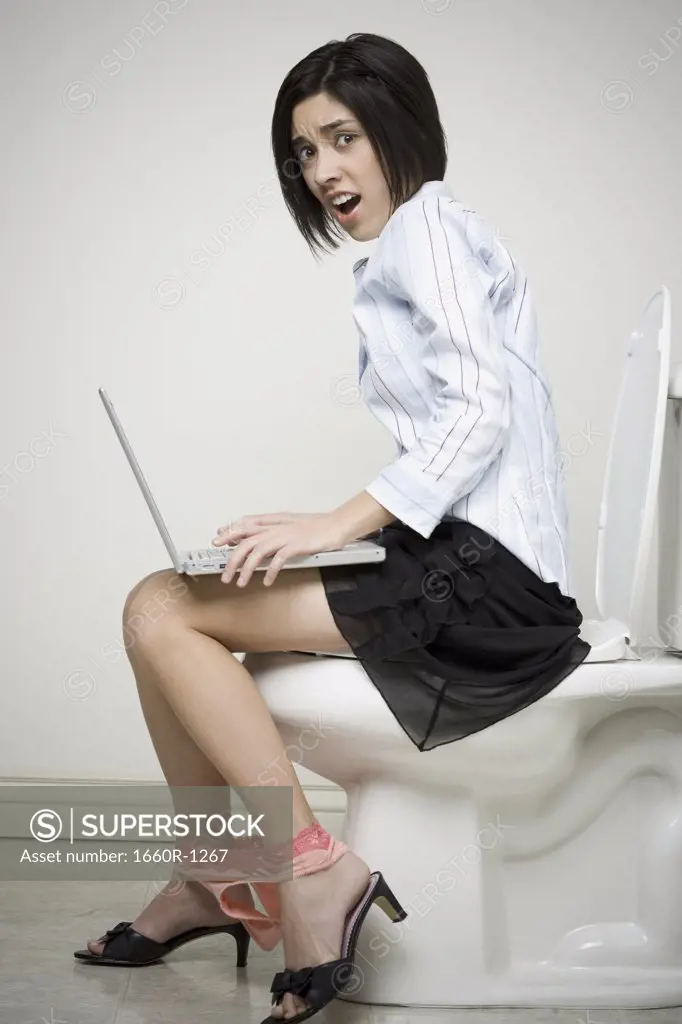 Portrait of a businesswoman sitting on a toilet with a laptop