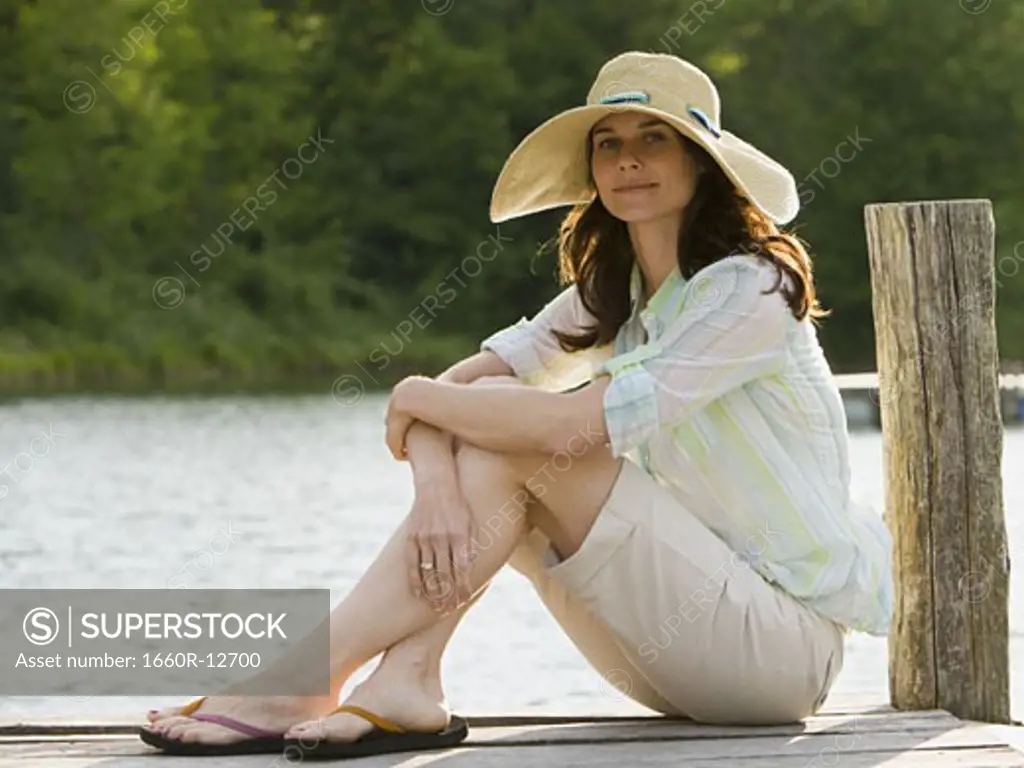 Portrait of a woman wearing a straw hat and sitting on a pier