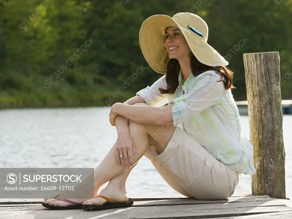 Profile of a woman wearing a straw hat and sitting on a pier