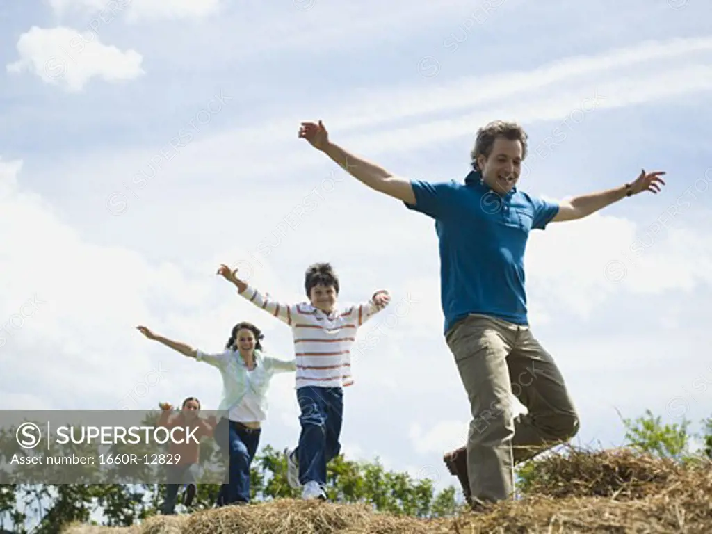 Low angle view of a man and a woman jumping with their children on hay bales
