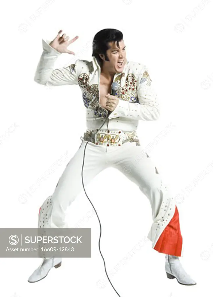 An Elvis impersonator singing into a microphone and jumping