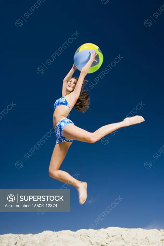 Profile of a young woman holding a beach ball and jumping