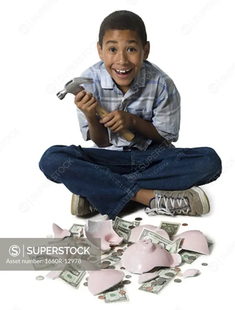 Portrait of a boy holding a hammer with a broken piggy bank in front of him