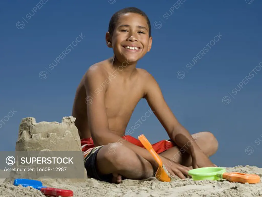 Portrait of a boy sitting beside a sand castle