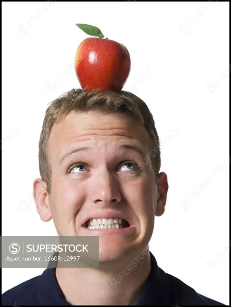 Close-up of a young man clenching his  teeth with an apple on his head