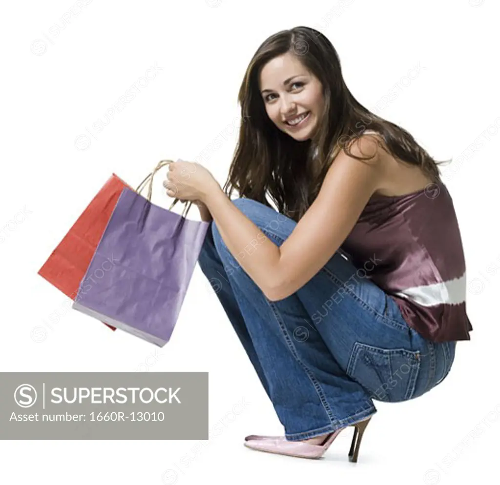 Portrait of a young woman crouching and holding shopping bags