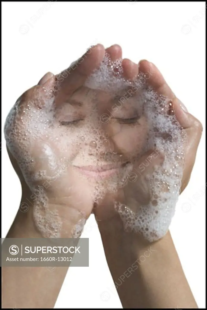 Reflection of a young woman's face in soap suds in her hands